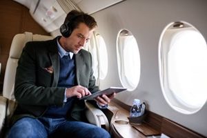 businessman on plane wearing headphones looking at tablet