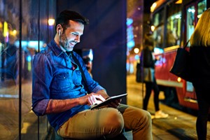 man sitting outside in city at night on laptop