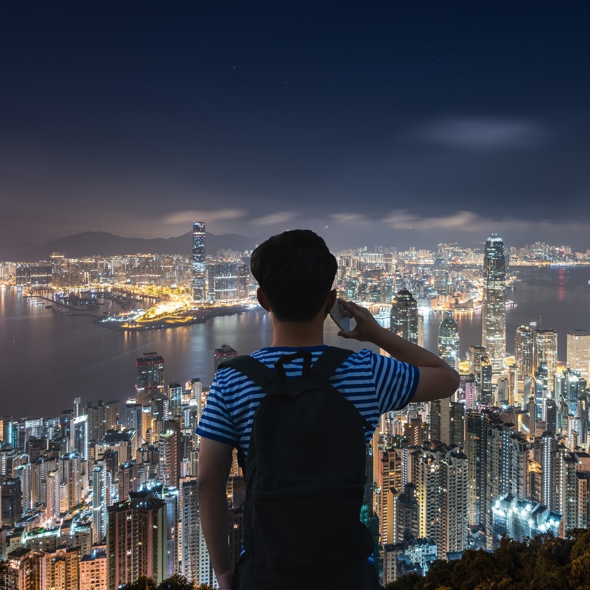 boy on cellphone overlooking lite up city at night