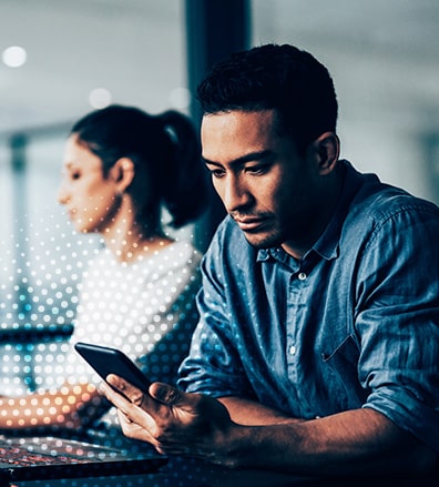 man looking at phone, woman working on laptop